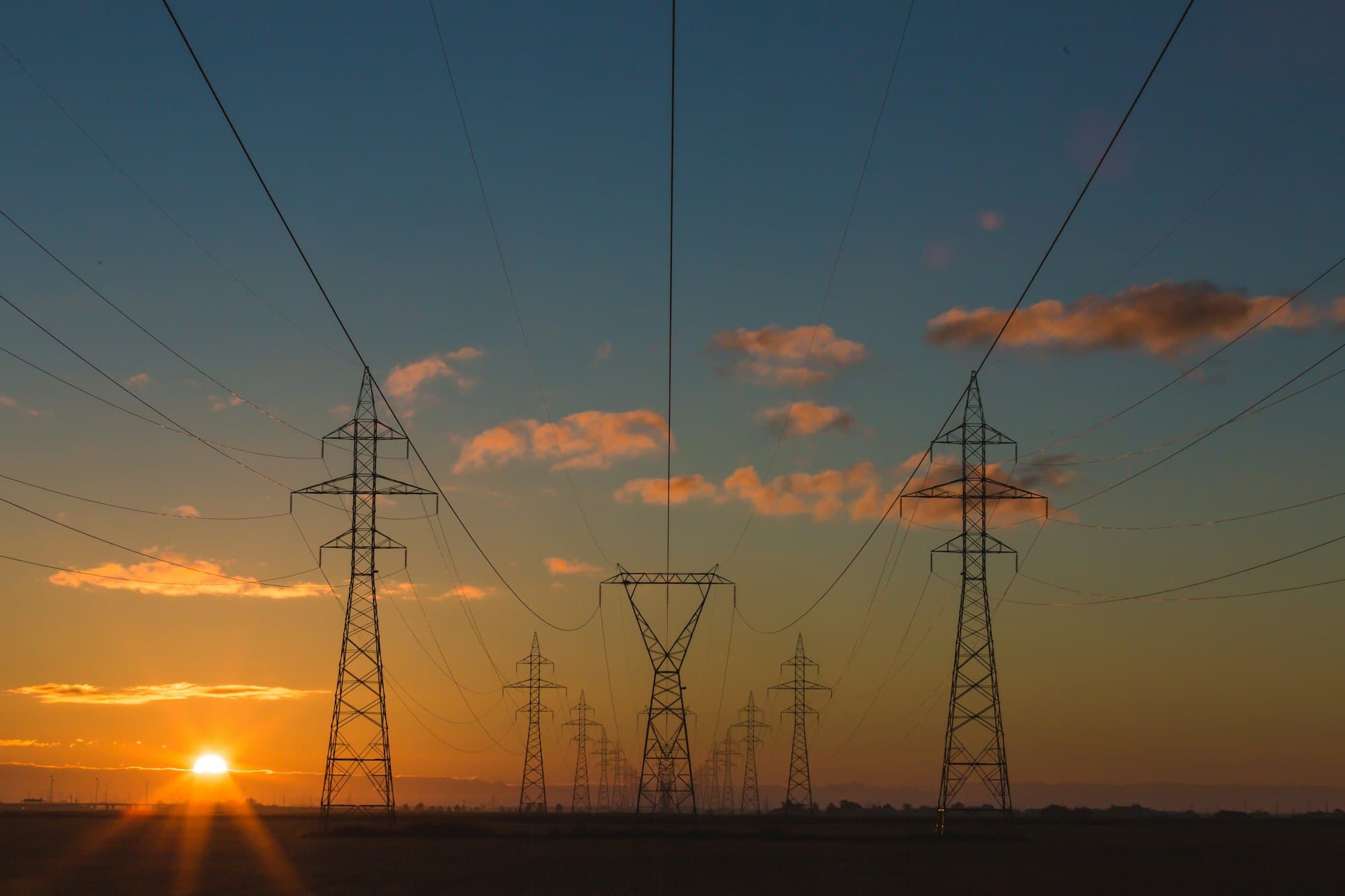 Electricity transmission towers silhouetted against a low evening sun